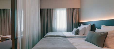 A hotel room with two beds, a large window with curtains, a headboard, and a bedside table.