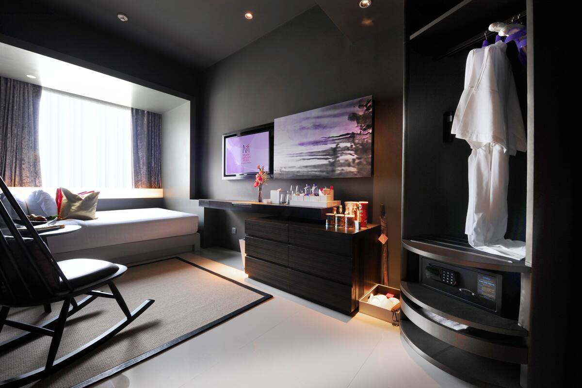 A modern hotel room with a sofa, a TV, a microwave, and a window with curtains.