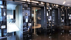 Un moderno vestíbulo de hotel con estanterías negras que exhiben varios objetos, un panel de vidrio y un suelo limpio y reflectante.