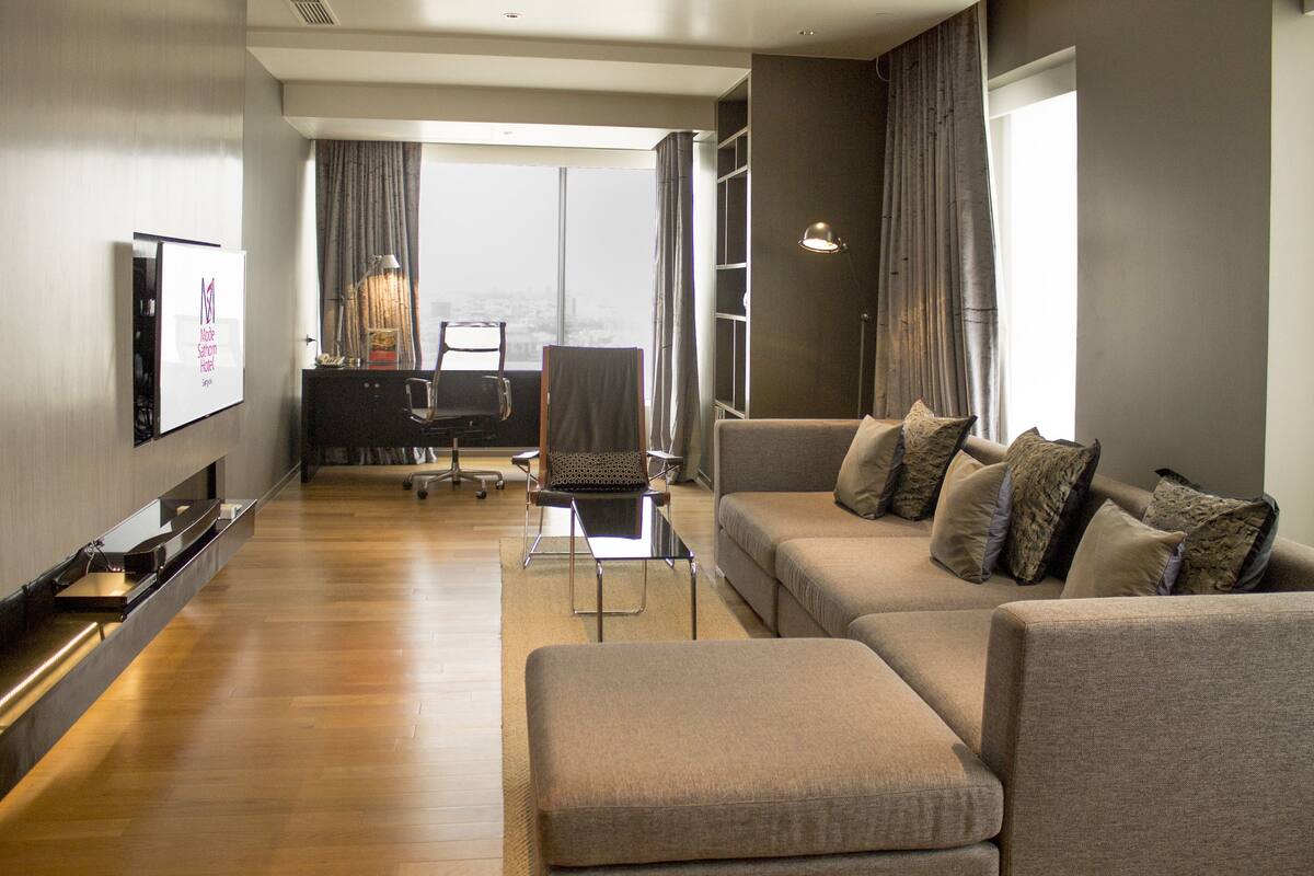 A modern living room with a sofa, ottoman, and a flat-screen TV mounted on the wall.
