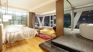 Habitación de hotel moderna con cama, zona de estar, vista nocturna de la ciudad y balcón.