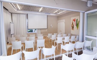 Uma sala de conferências com cadeiras brancas dispostas em fileiras, um quadro branco e uma tela de projeção.