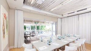 A conference room with a long table, white chairs, and a view of an outdoor patio. - Quarry Lake Inn (East London)