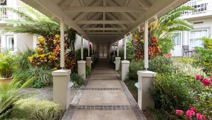 A covered walkway with a tiled floor, flanked by lush greenery and potted plants. - Quarry Lake Inn (East London)