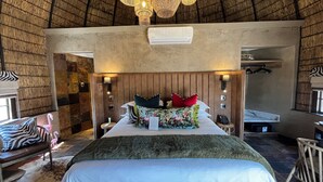 A room with a bed, a chandelier, a wall-mounted air conditioner, and a small table with a lamp.