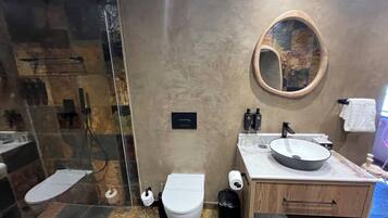 A modern bathroom with a glass shower enclosure, a toilet, a sink with a round mirror, and a wooden vanity.