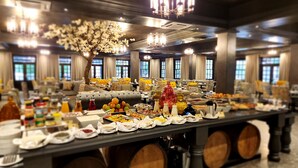 A buffet setup with various food items and beverages, a chandelier, and large windows in the background.