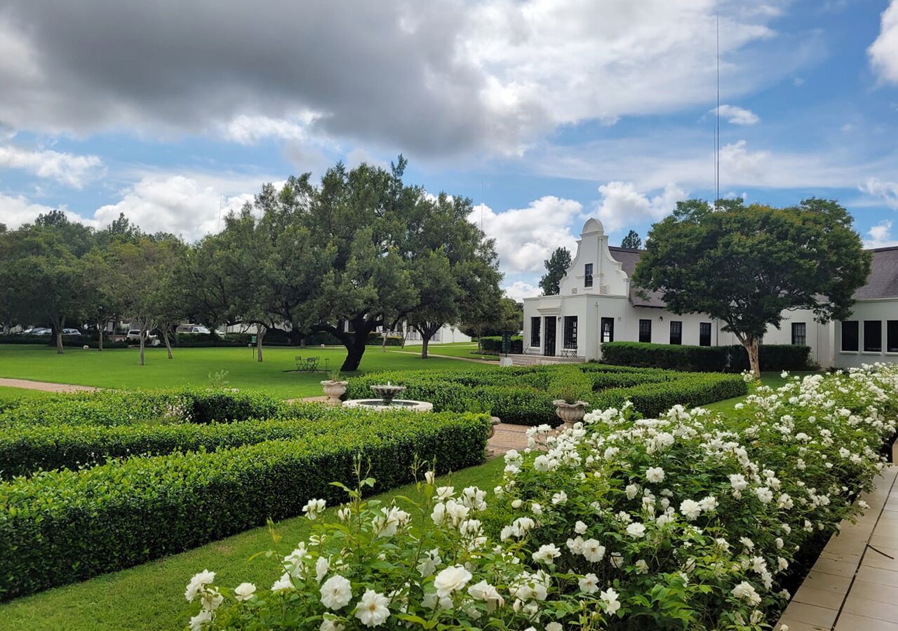 A white building with a dome, surrounded by well-manicured gardens and trees.