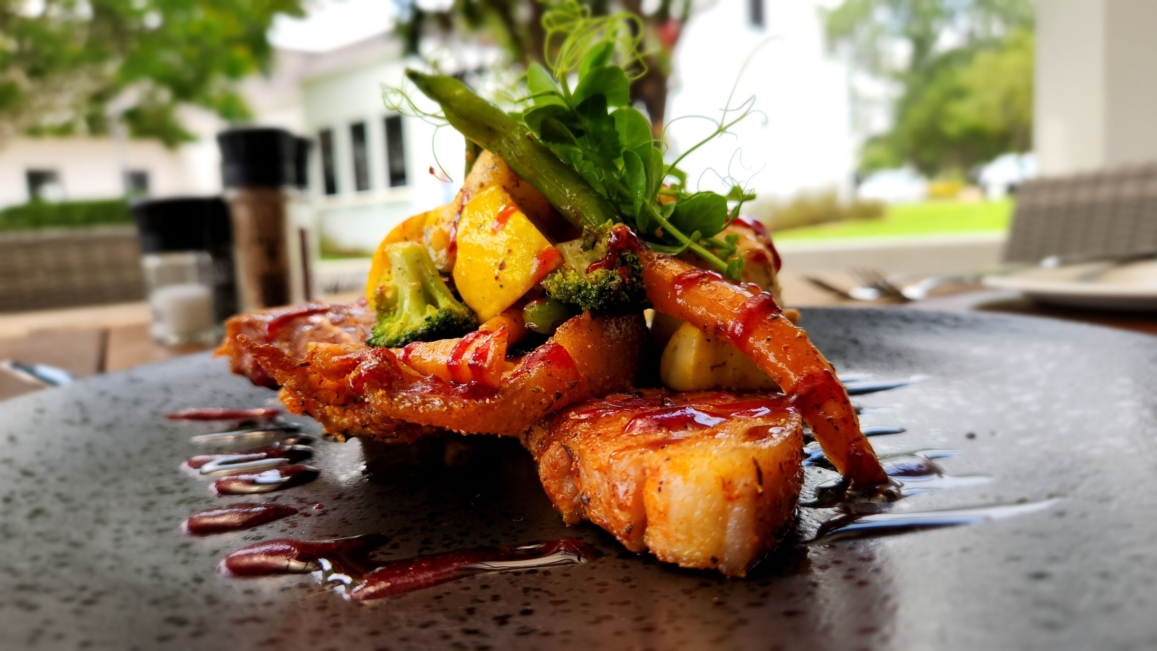 Un plat composé de différentes sortes de légumes et de viande, servi dans une assiette foncée accompagnée d’une sauce.