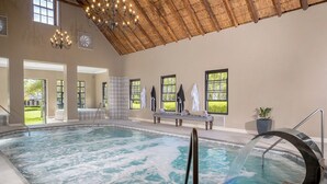 An indoor swimming pool with a thatched roof, large windows, and a bench with towels.
