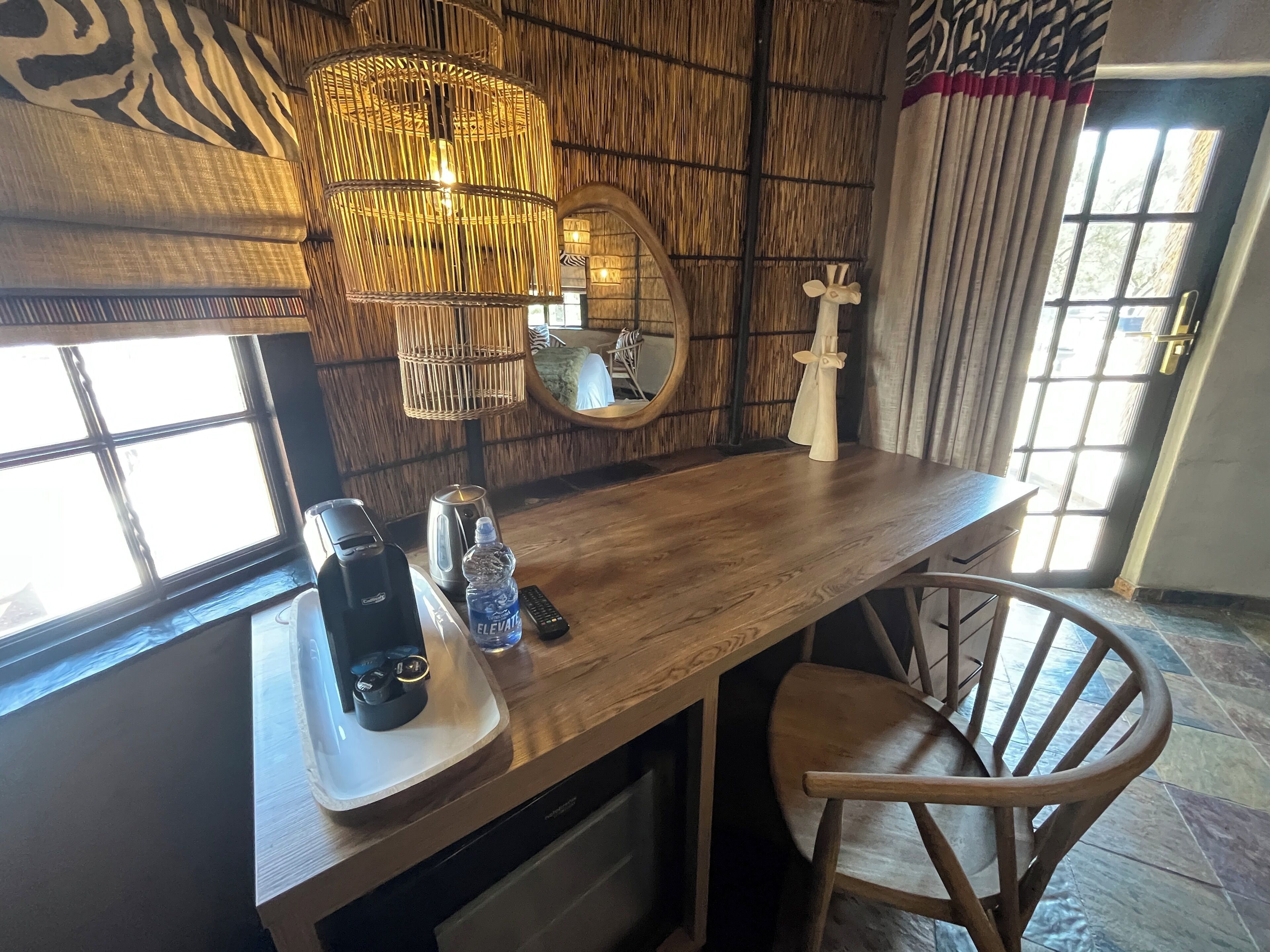 Una zona de bar con barra de madera, una cafetera, una botella de agua, un espejo y una silla.