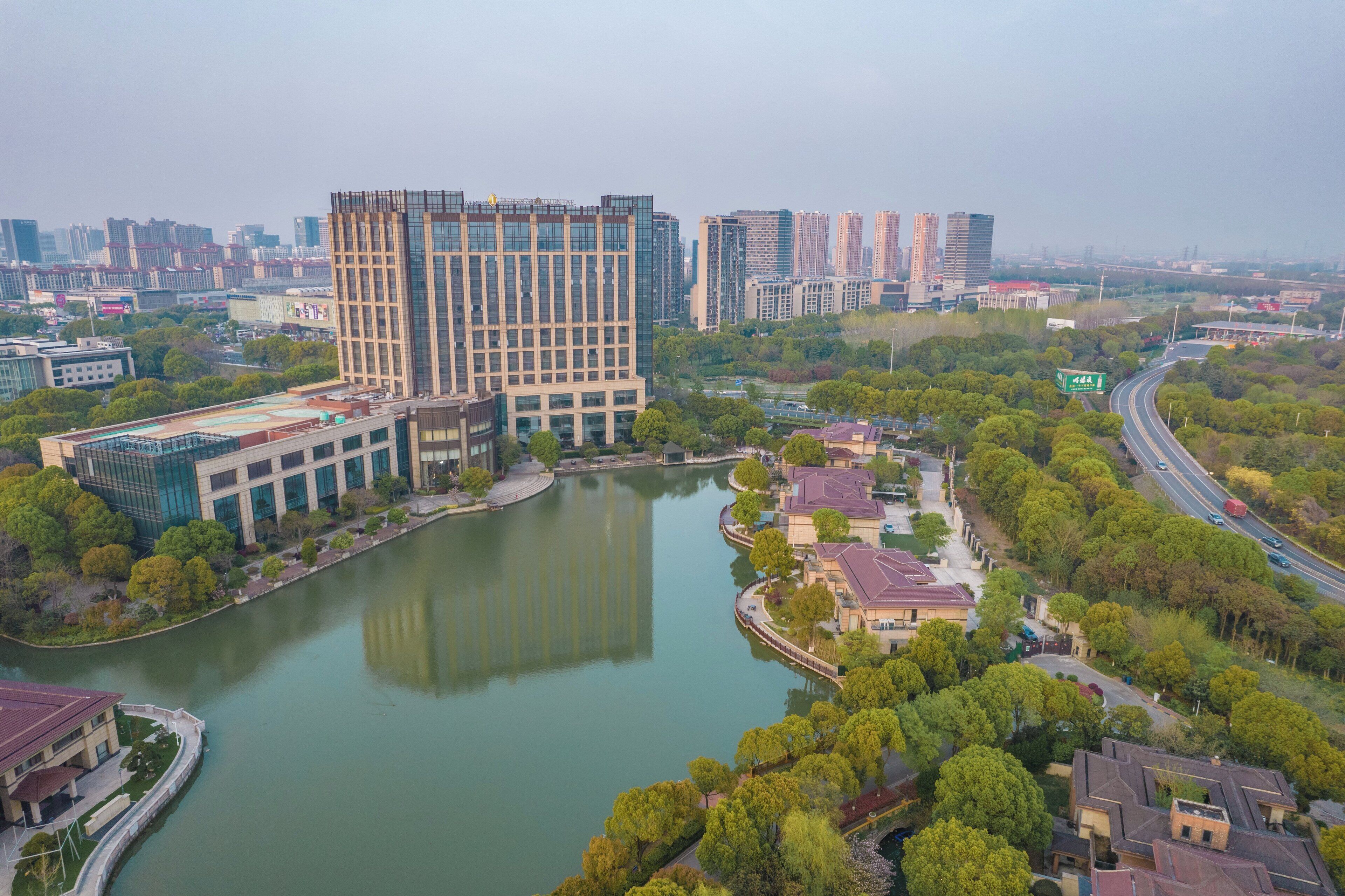 A high-rise building with a modern glass facade, surrounded by a river and greenery.
