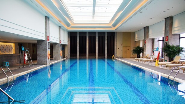Una piscina interior con agua azul cristalina, un techo con tragaluces y sillones de descanso a los lados.