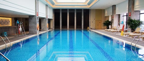 Una piscina interior con agua azul cristalina, un techo con tragaluces y sillones de descanso a los lados.