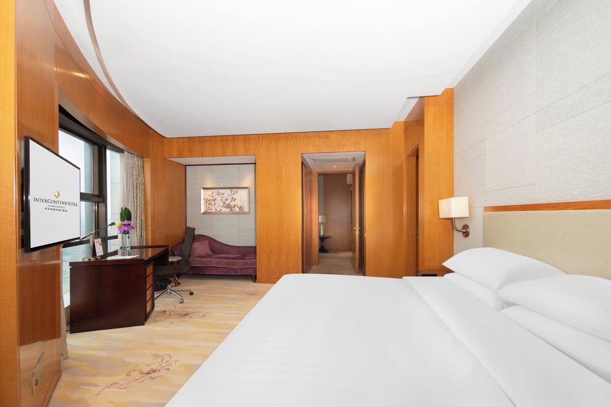 Habitación de hotel con una cama grande, un escritorio con computadora, una silla y un televisor.