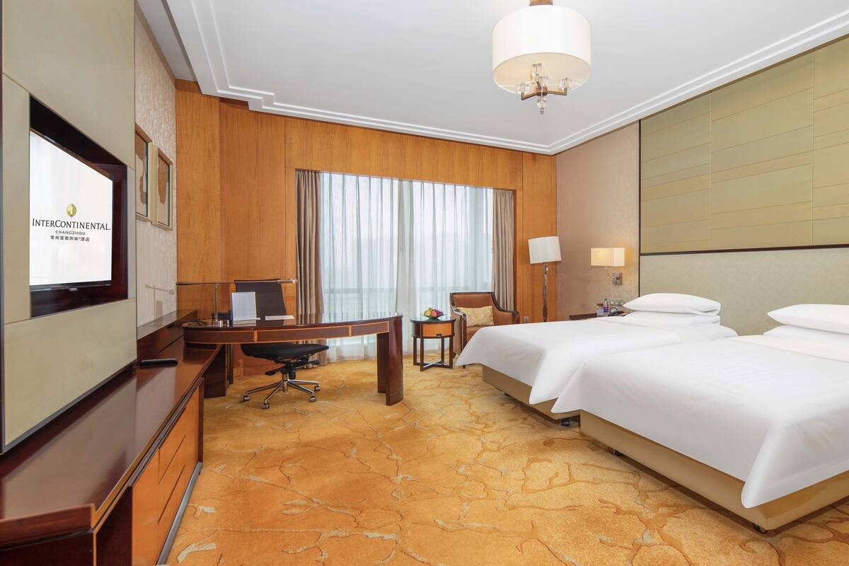 Una habitación de hotel con una cama grande, un escritorio, una silla, un televisor y una araña.