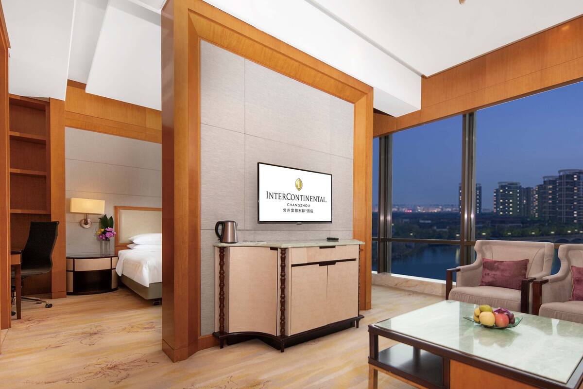 Una habitación de hotel con un ventanal grande, televisión, escritorio, silla y cama.