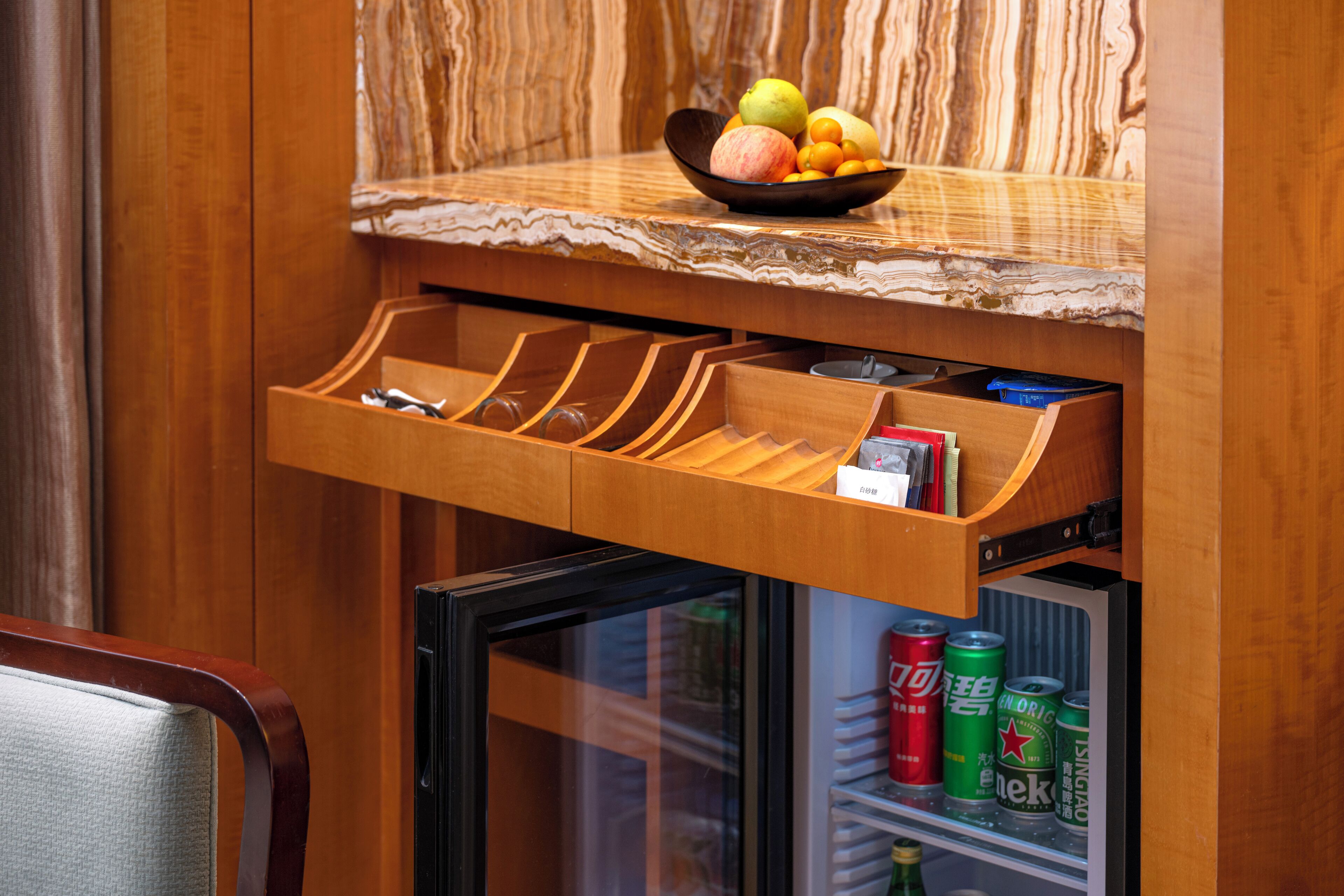A kitchen with a wooden countertop, a fruit bowl, a drawer organizer, and a mini-fridge with beverages.