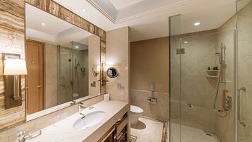 A modern bathroom with a large mirror, dual sinks, a glass-enclosed shower, and marble walls.