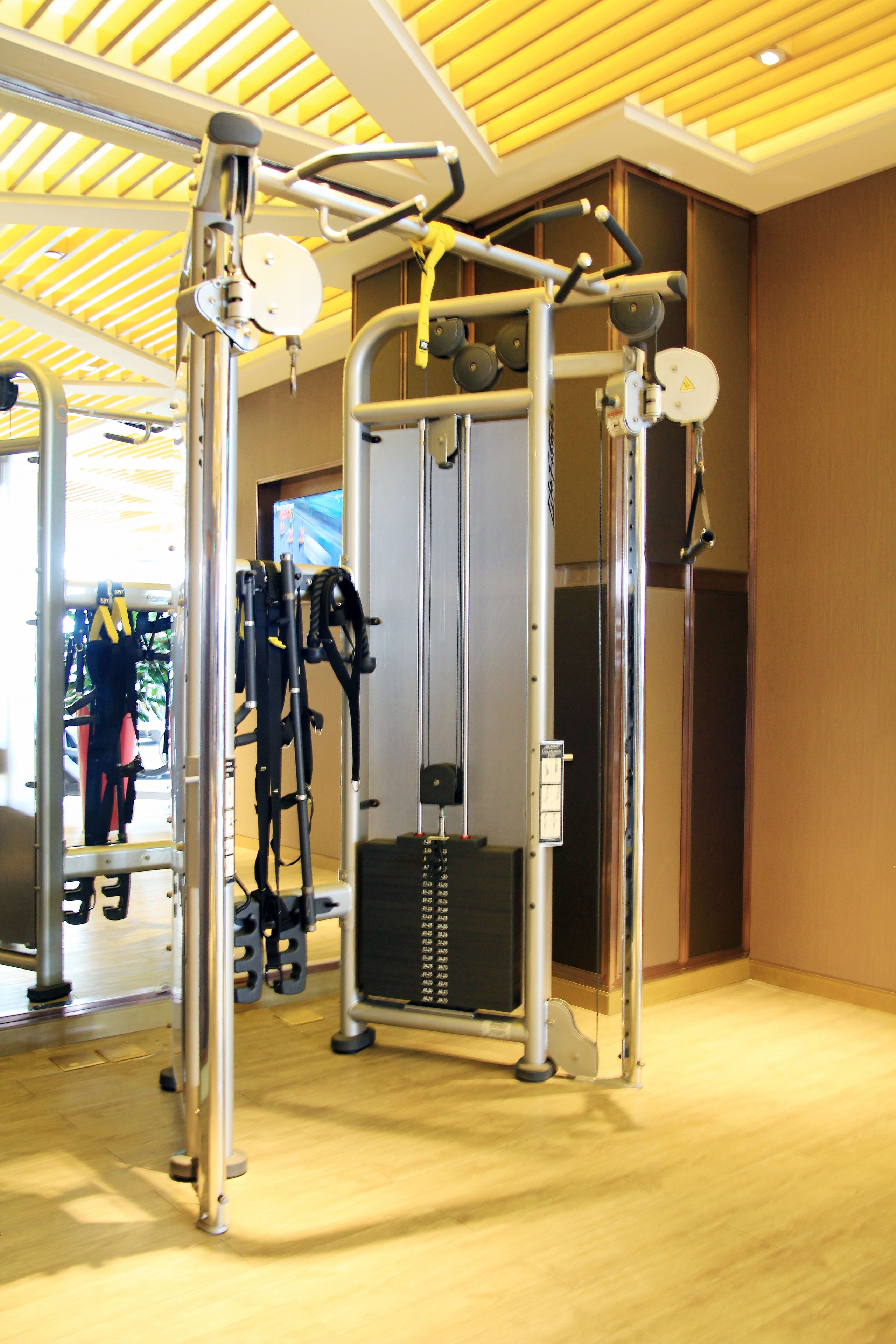 Een sportschool met diverse fitnessapparaten, een houten vloer en een plafond met houten latten.