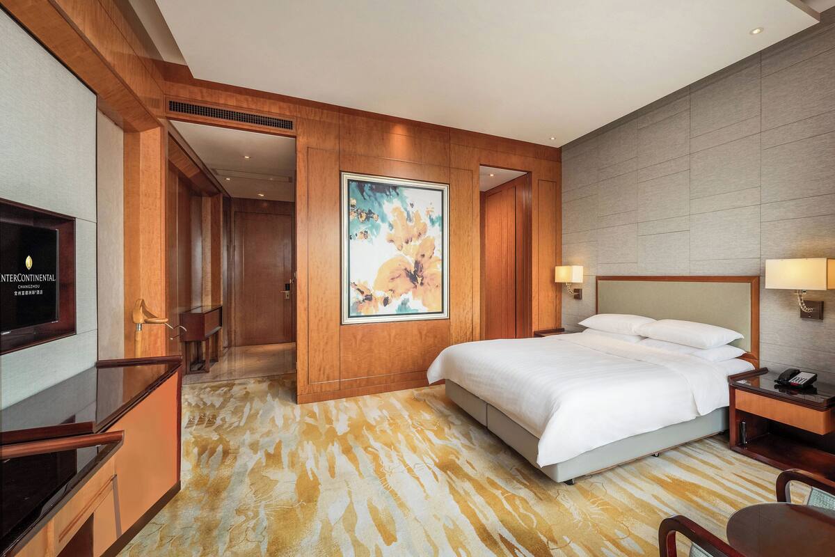 Una habitación de hotel con cama, mesita de noche, lámpara y un cuadro en la pared.