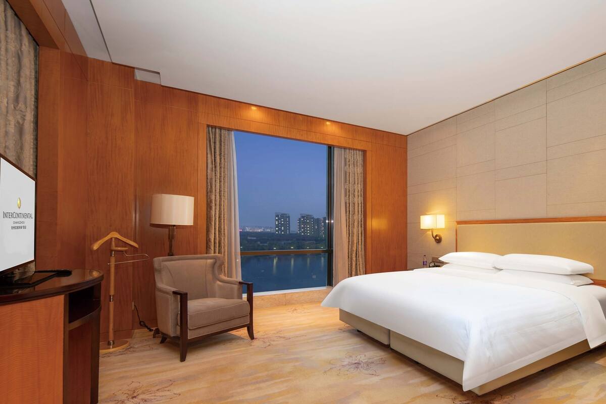 Habitación de hotel con una cama grande, un escritorio, una silla y vistas a la ciudad.