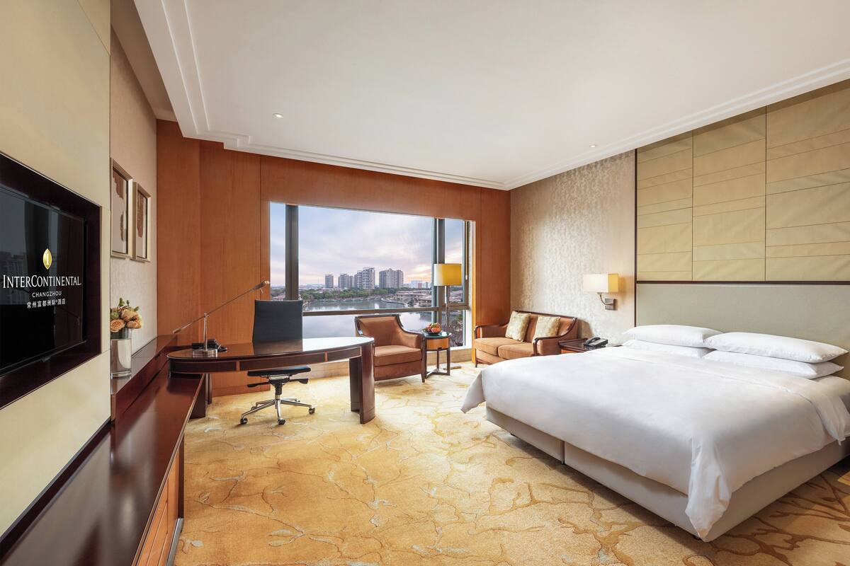 Habitación de hotel con una cama grande, un escritorio con silla, televisión y vistas a la ciudad.