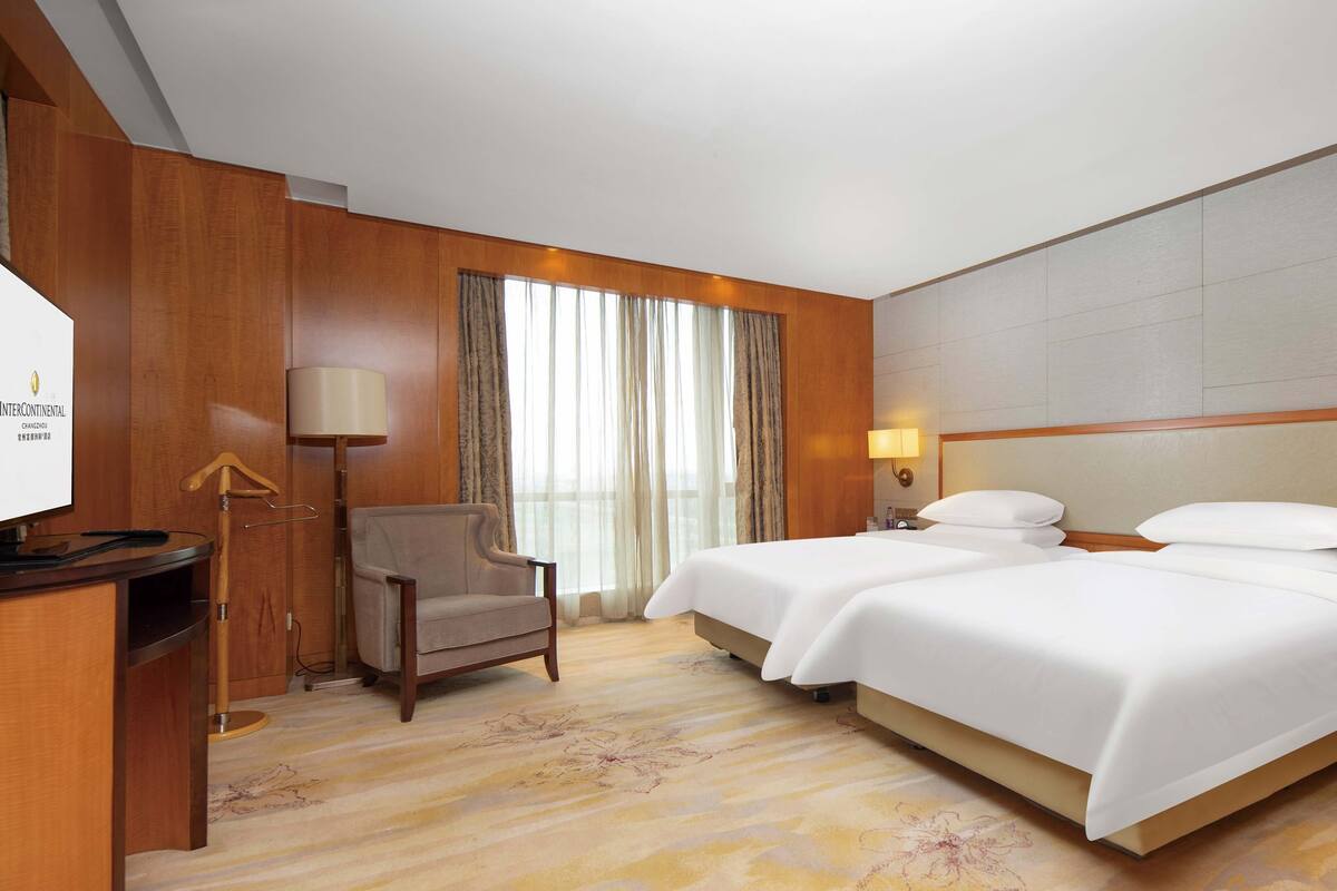 Habitación de hotel con dos camas, un escritorio, una silla, un televisor y una ventana con cortinas.