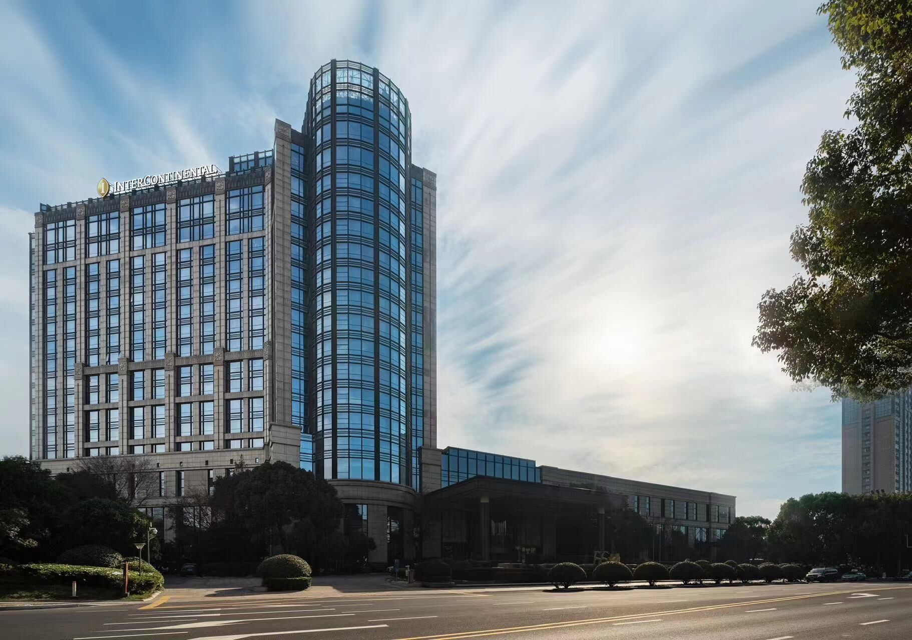 A modern hotel with a curved glass facade, a classic building with a stone facade, and a well-maintained landscaped area.