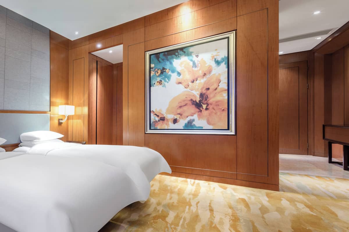 Habitación de hotel con una cama grande, una lámpara de pared, una obra de arte floral enmarco y paneles de madera.