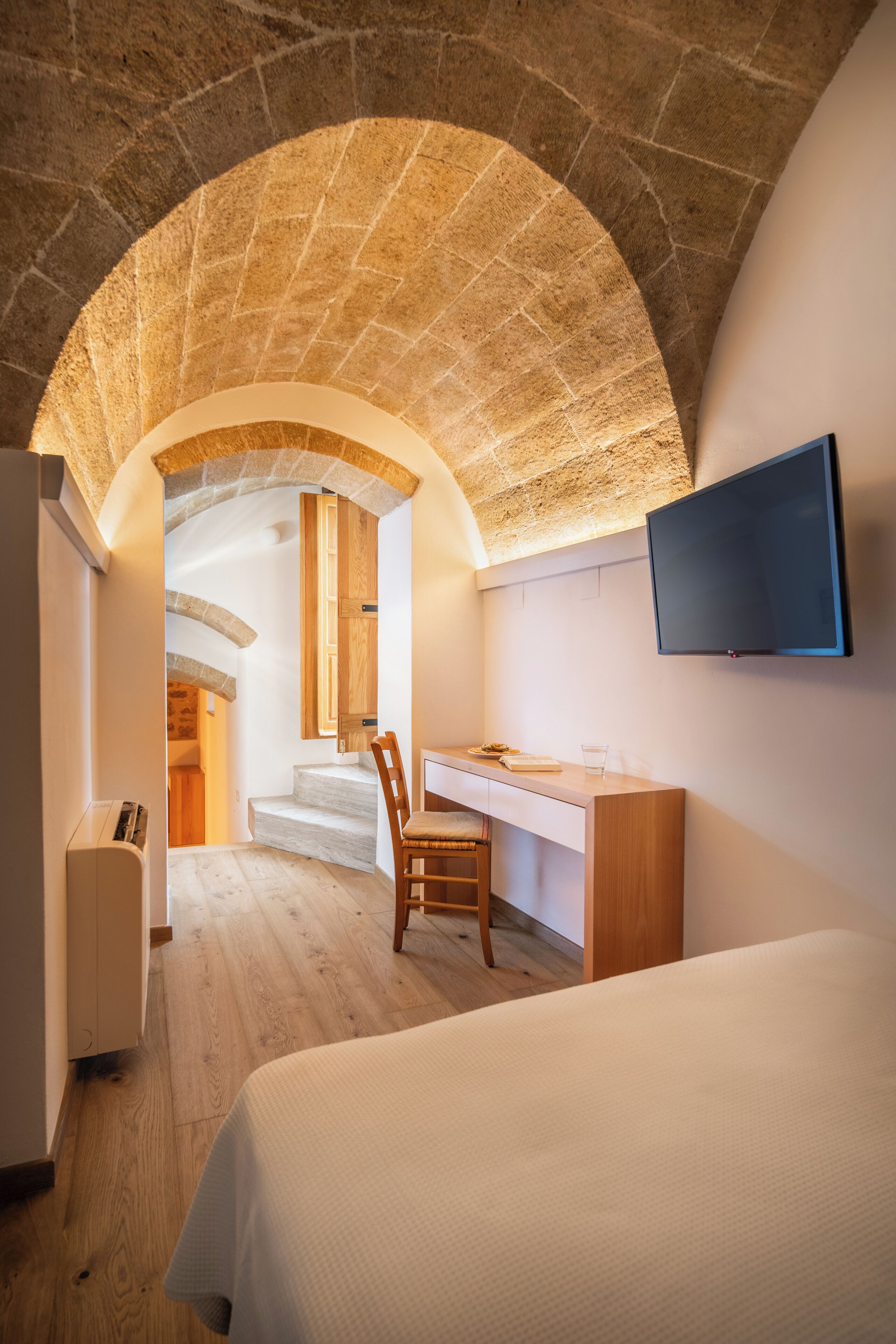 A bedroom with a bed, a desk, and a TV. There is a staircase leading to an upper level.
