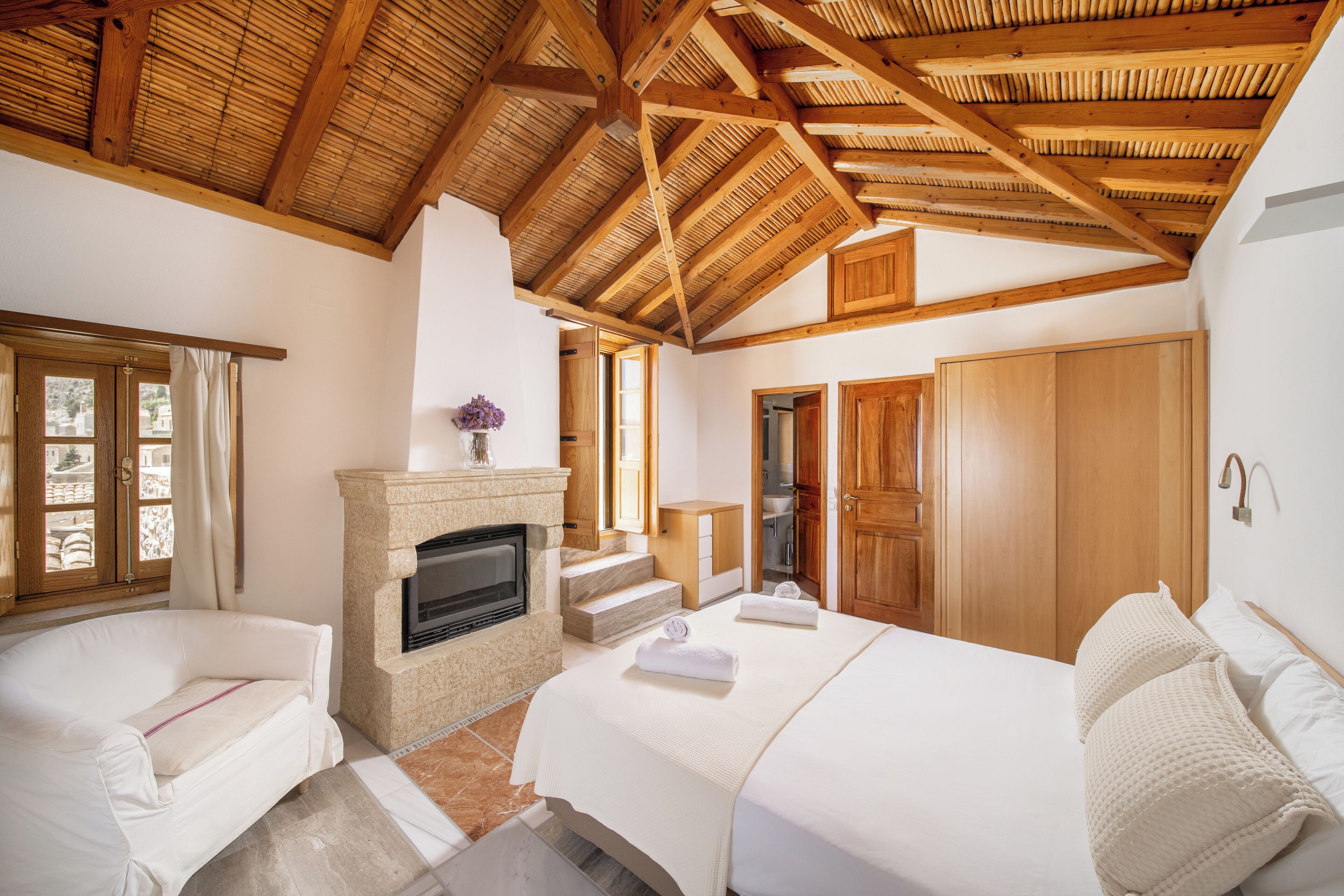 Un dormitorio con chimenea, vigas de madera en el techo, un sofá y una cama.
