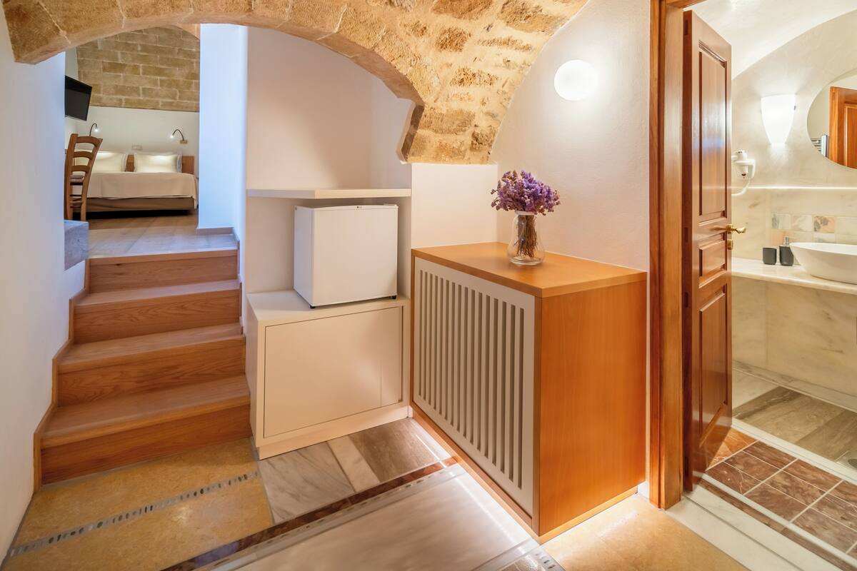 A modern bathroom with a stone archway, a wooden staircase, and a white radiator.