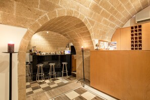 A bar area with stools, a checkered floor, and a stone archway. - Bastione Malvasia Hotel (Monemvasia)