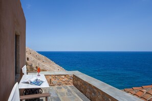 Una terraza con una mesa, un libro y una vela. La terraza da a una escalera de piedra y al mar.
