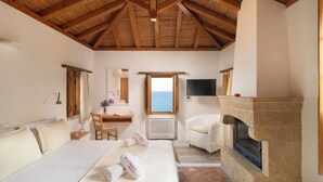 Une chambre avec un grand lit, un bureau, une chaise, une cheminée et une vue sur la mer.