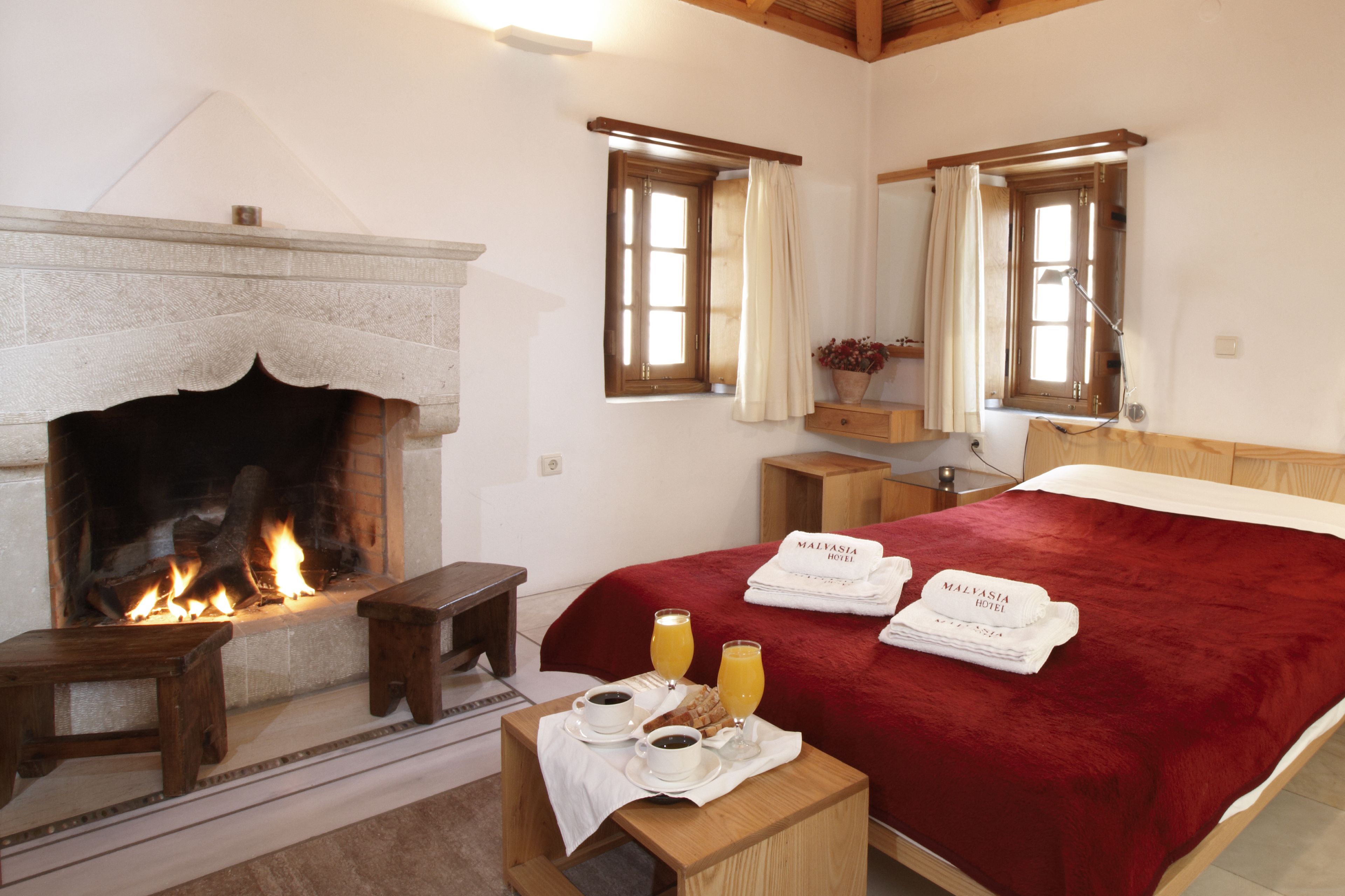 A bedroom with a fireplace, a bed with a red blanket, two bedside tables, and a nightstand with a lamp.