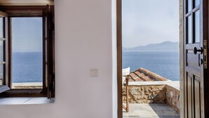 Une porte ouverte donnant sur un balcon avec vue sur la mer et les montagnes.
