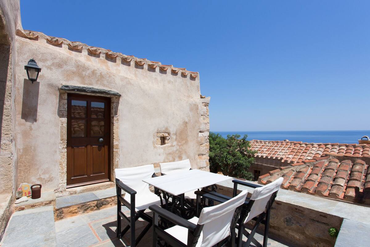 A terrace with a table and chairs, a door, and a view of the sea.
