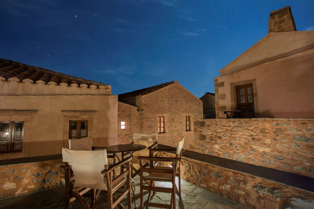 A stone-walled courtyard with a table and chairs, under a starry night sky.