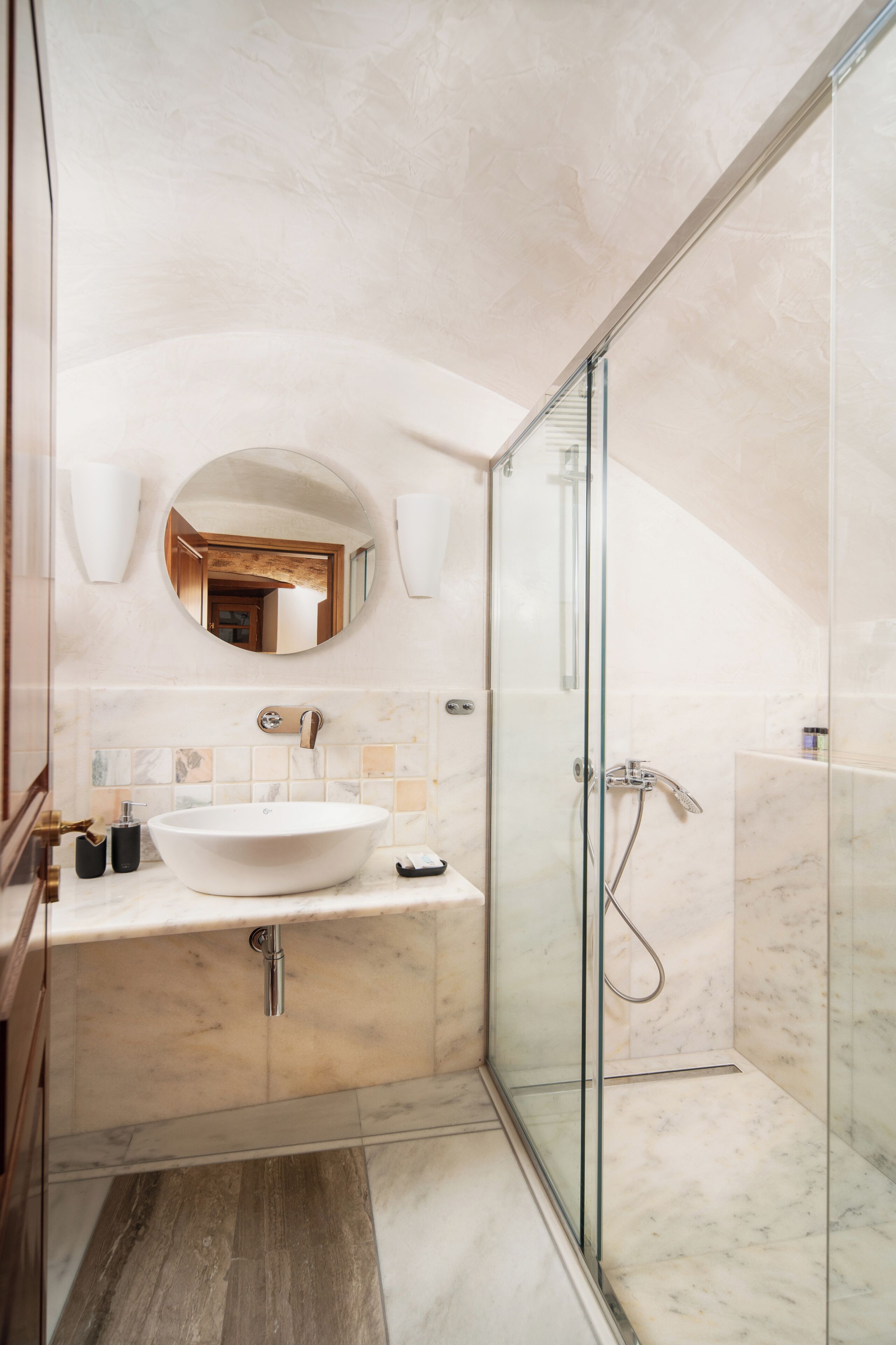 Un baño moderno con un lavamanos ovalado grande, una ducha con cerramiento de vidrio y un piso de baldosas de mármol.