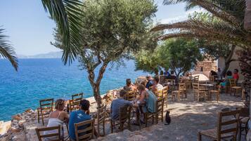 Un espace extérieur aménagé avec des tables et des chaises en pierre, situé sur la côte et offrant une vue sur la mer.