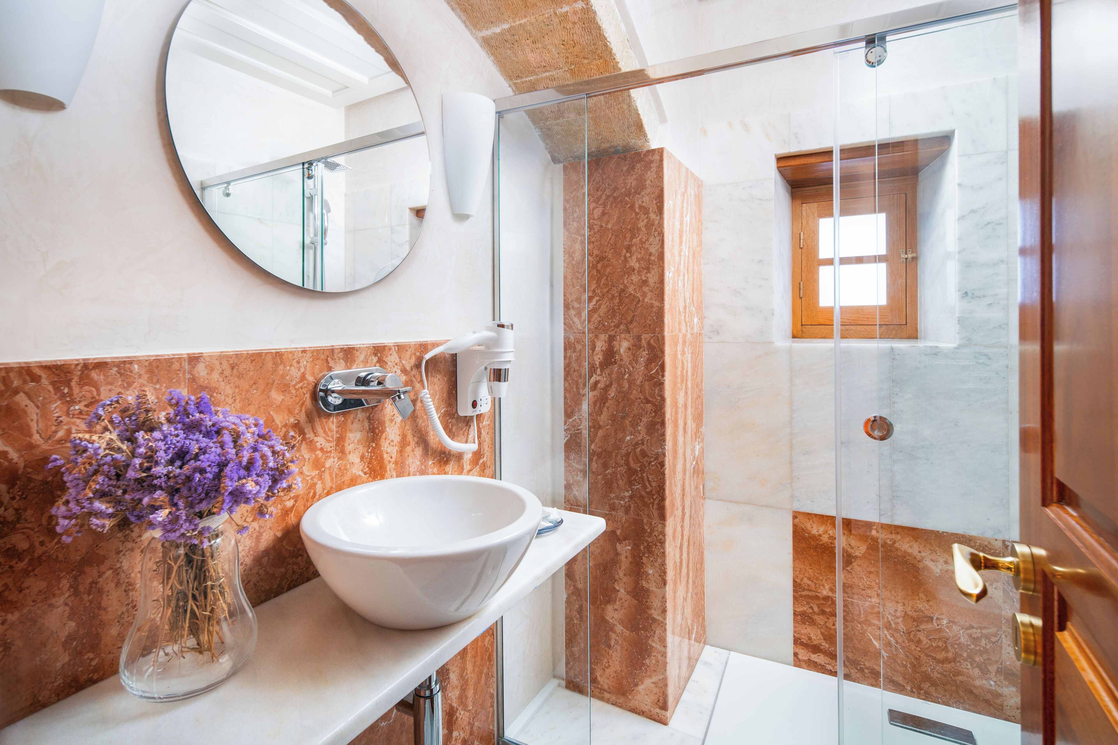 A bathroom with a white sink, a vase of purple flowers, a mirror, and a glass shower enclosure.