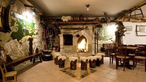 A rustic interior with a stone wall, a fireplace, wooden stools, and a dining area. - LH Hotel Paradiso (Pescasseroli)