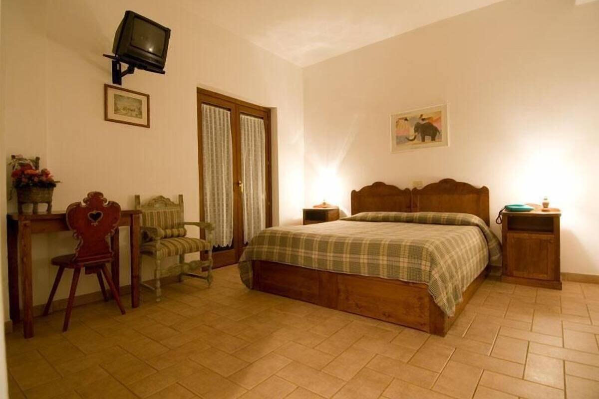 A bedroom with a wooden bed, a desk with a chair, a television, and a picture on the wall.