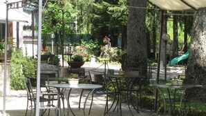 An outdoor patio area with round tables and chairs, surrounded by trees and potted plants. - LH Hotel Paradiso (Pescasseroli)