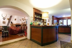 Uma área de bar com balcão de madeira, prateleiras com garrafas e uma luminária.