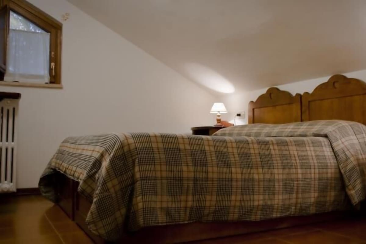 Quarto com uma cama, mesa de cabeceira, abajur e janela com cortina.
