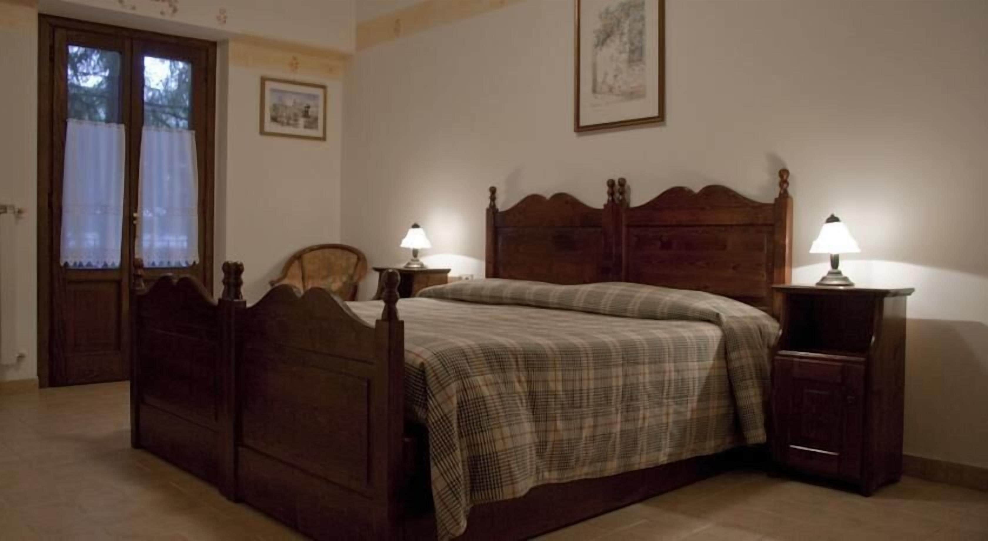 Une chambre à coucher avec un lit en bois, deux tables de chevet avec des lampes, une chaise, une porte et un tableau encadré au mur.