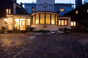 A hotel with a circular glass facade, a stone courtyard, and a snow-covered entrance. - LH Hotel Paradiso (Pescasseroli)